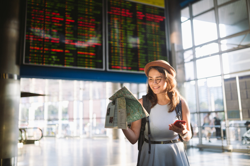 Junge Frau steht mit Landkarte am Flughafen