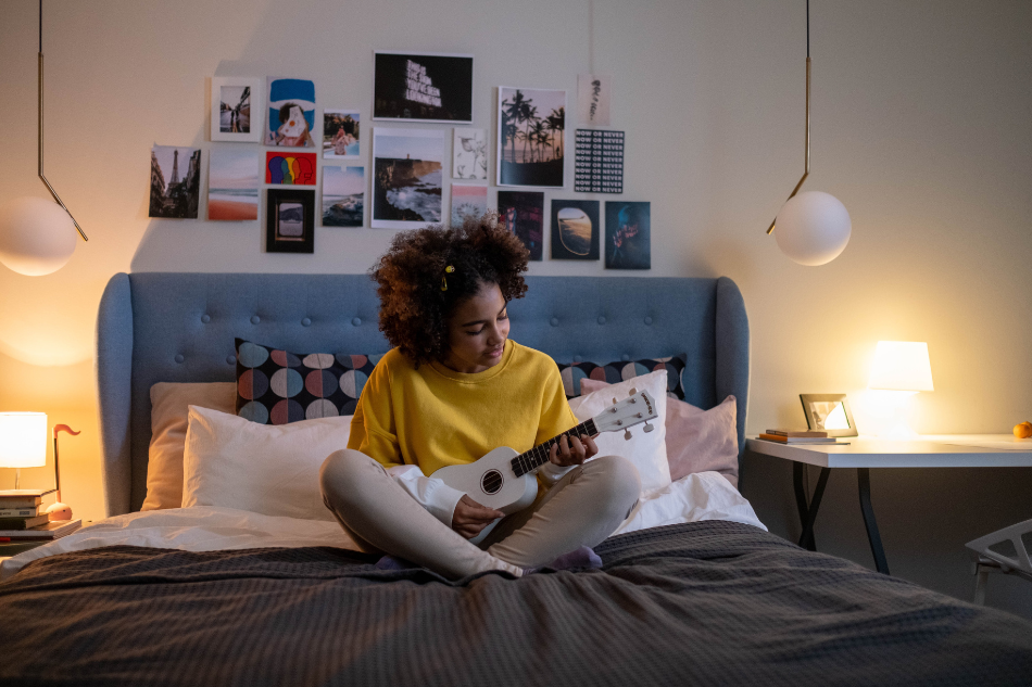 Mädchen sitzt mit einer Gitarre auf ihrem Bett. 