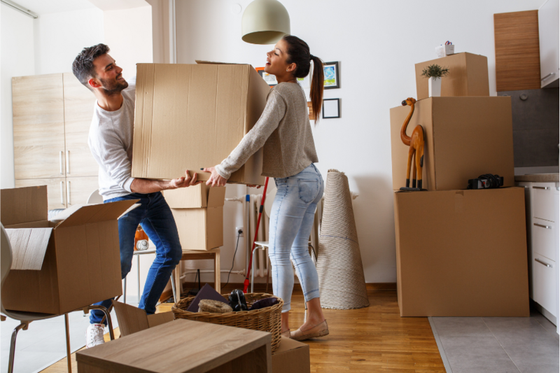 Ein Mann und eine Frau tragen einen Umzugskarton in die Wohnung. 