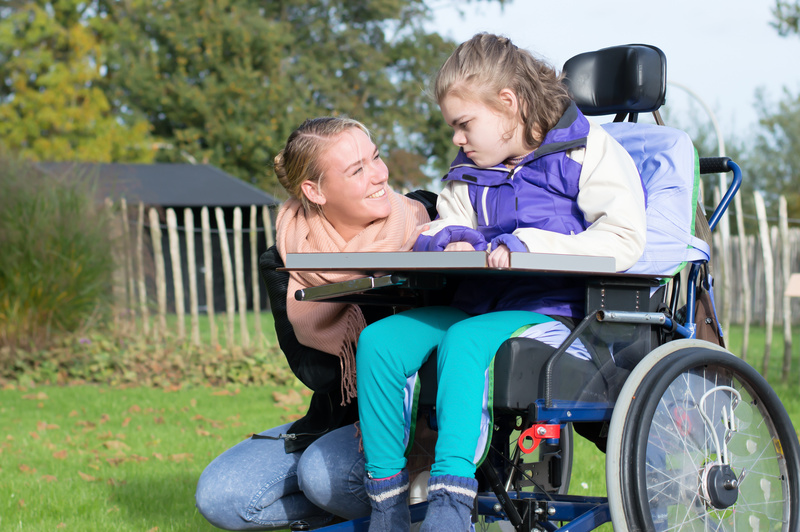 Heilerziehungspflegerin spricht mit Kind mit Behinderung im Rollstuhl