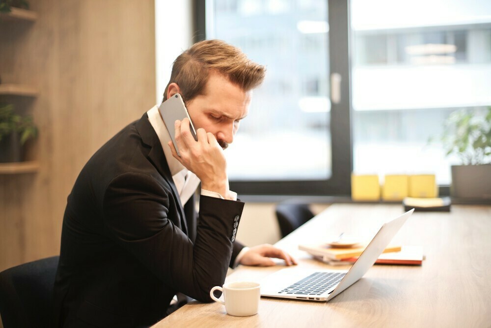 Ein Mann telefoniert mit seinem Smartphone und sitzt vor einem Laptop