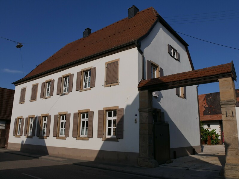 Das ehemalige reformierte Pfarrhaus in Iggelheim ist heute ein Ort für Begegnung. Die in die Sandsteingewände der Toreinfahrt eingemeißelten Ornamente sind noch zu erkennen. 
