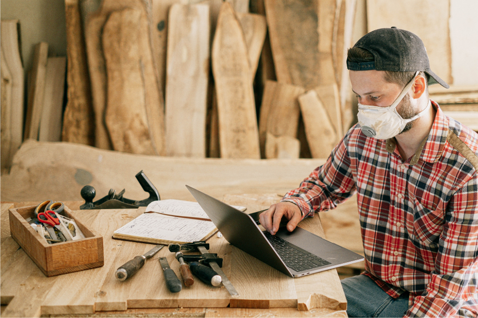 Mann sitzt mit einem Mundschutz vor einem Laptop. 