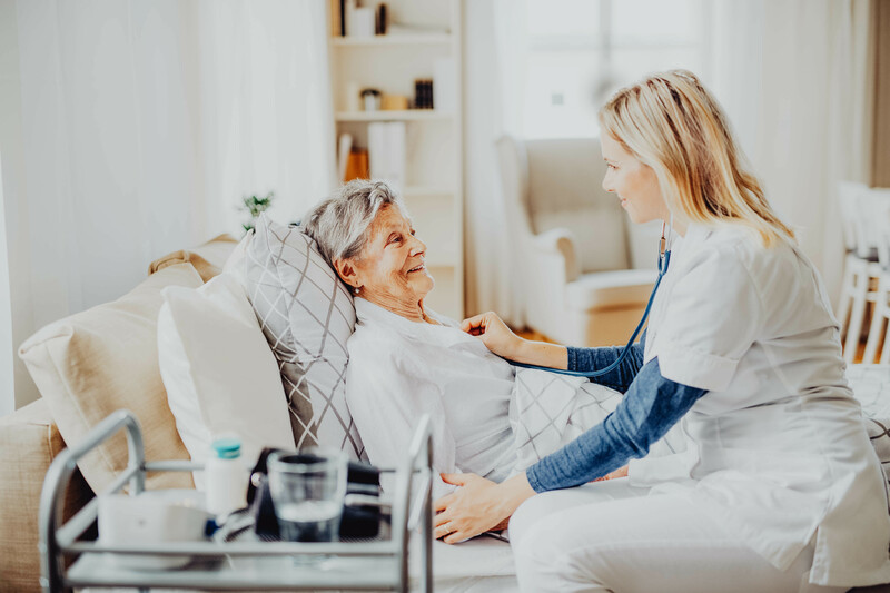 Pflegerin hört Herzschlag von Seniorin ab.